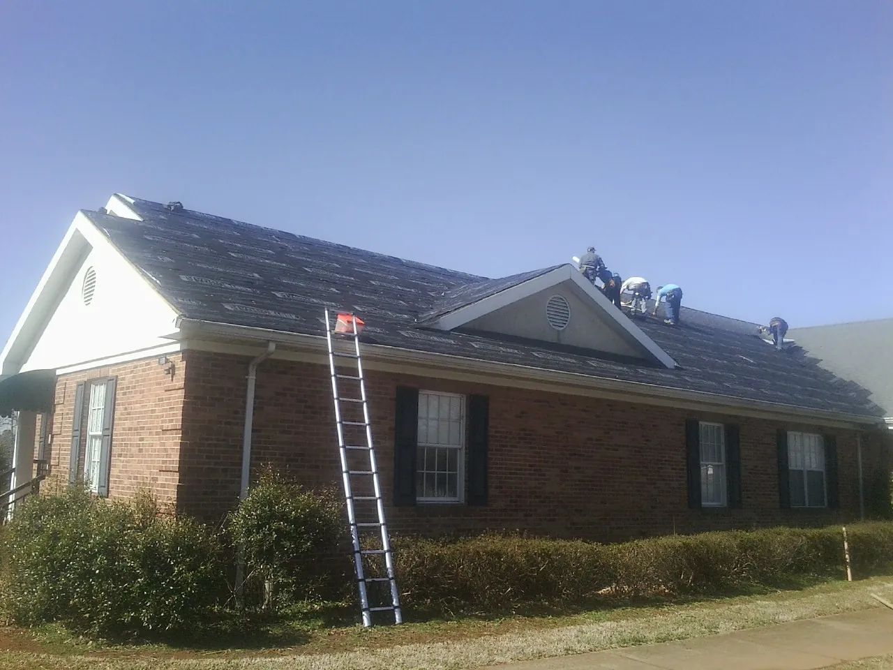 Crew tearing shingles off a brick ranch roof with a ladder set — Emergency Roof Repair work by our crew in Fletcher