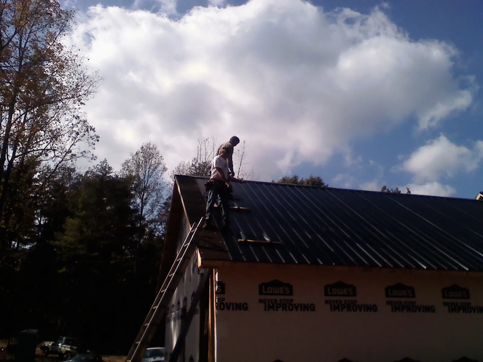 Roofer fastening dark metal panels high against a cloudy sky, from a Roof Inspection job in Fletcher